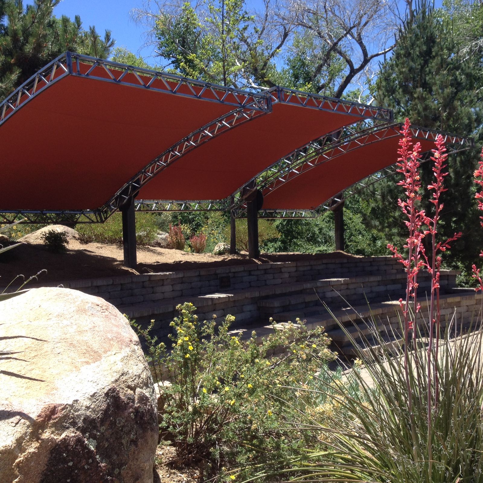 Arched steel-truss shade canopies with rust-orange fabric over a stone amphitheater in Northern Arizona